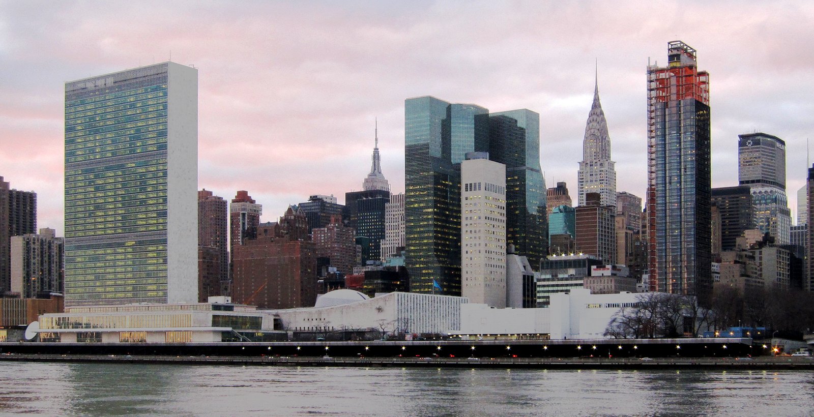 United Nations Headquarters beside the East River, with the New York skyline at dusk